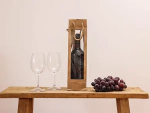 A bottle of wine in a kraft gift bag with two glasses and grapes