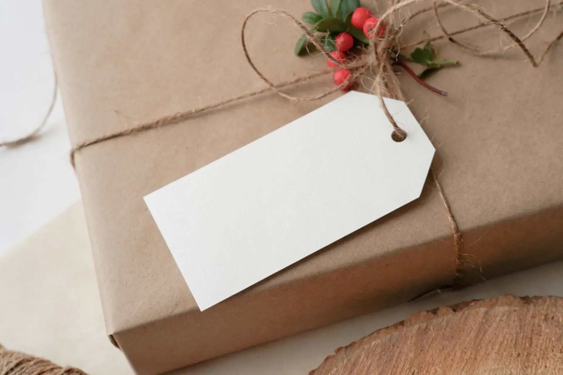 A gift wrapped in brown kraft paper, tied with twine and berries, with a blank gift tag
